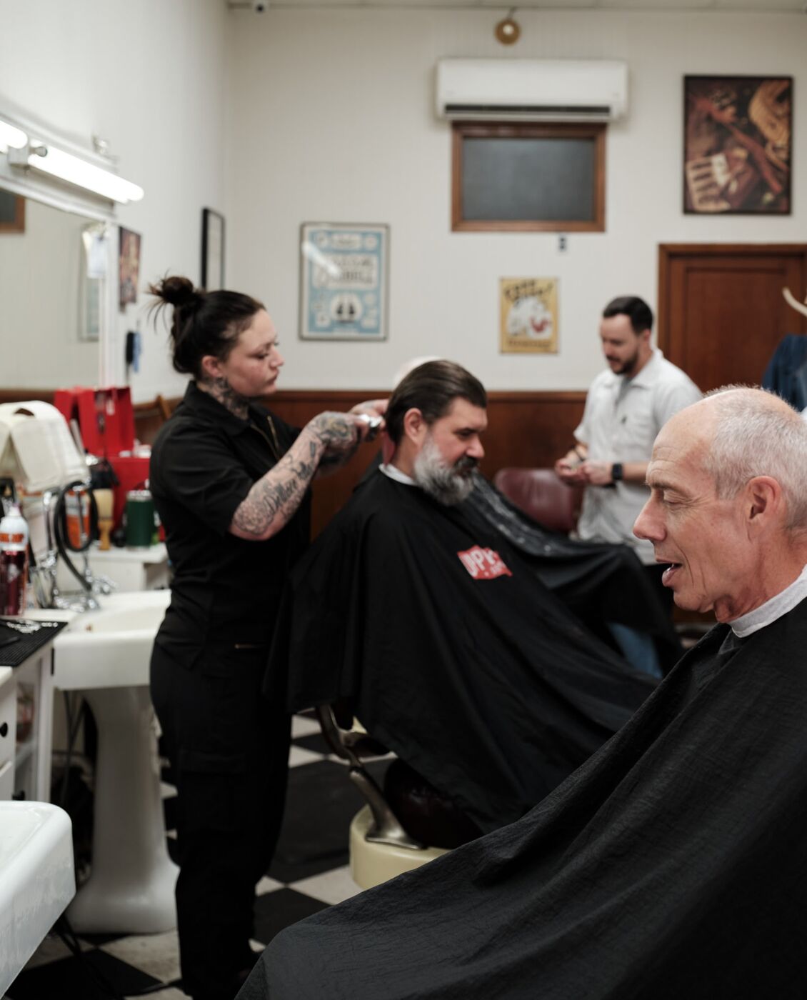 Two barbers cutting clients' hair inside Monty's Barber Shop